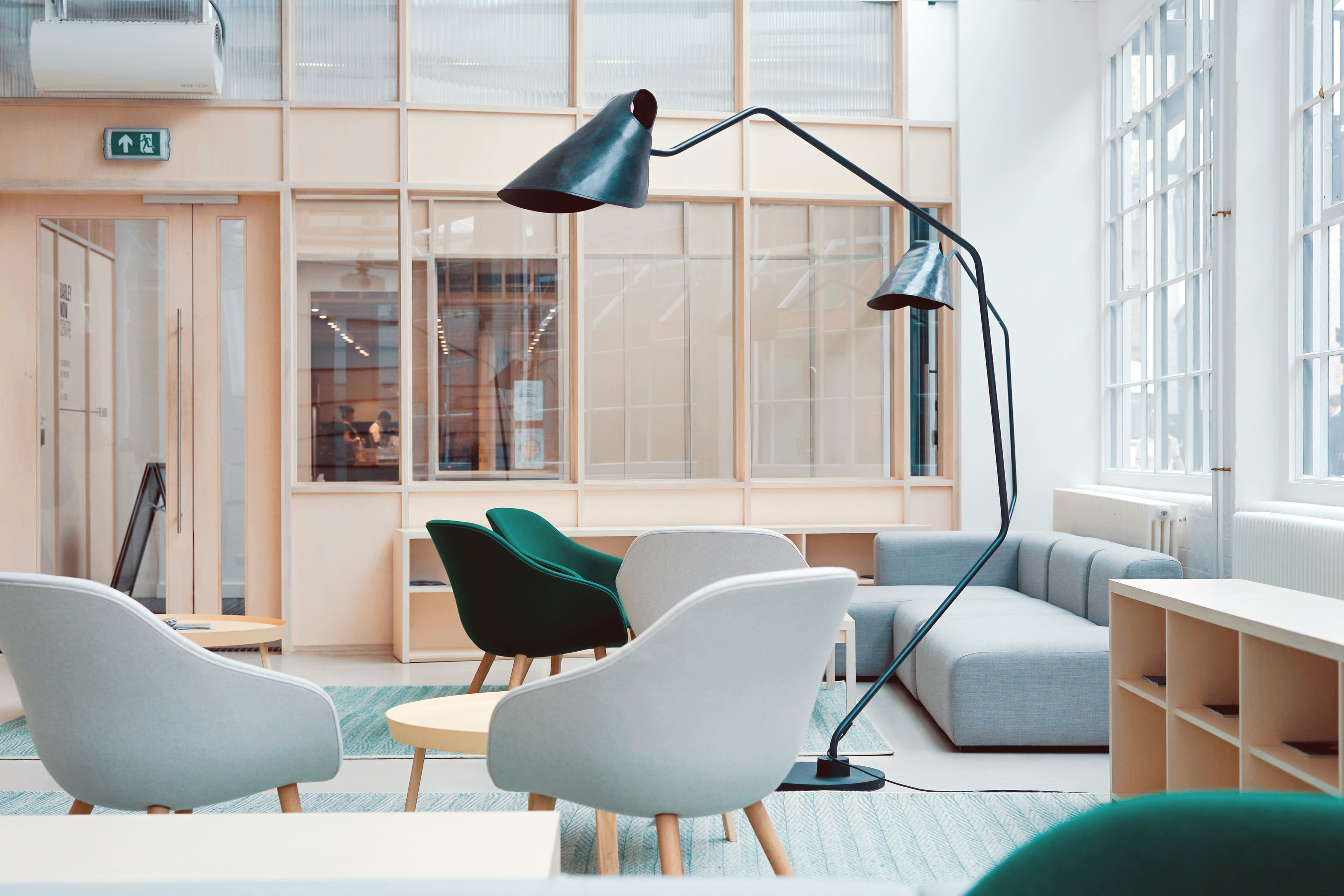 Bright modern lounge with grey and green armchairs, wooden tables, and natural window light